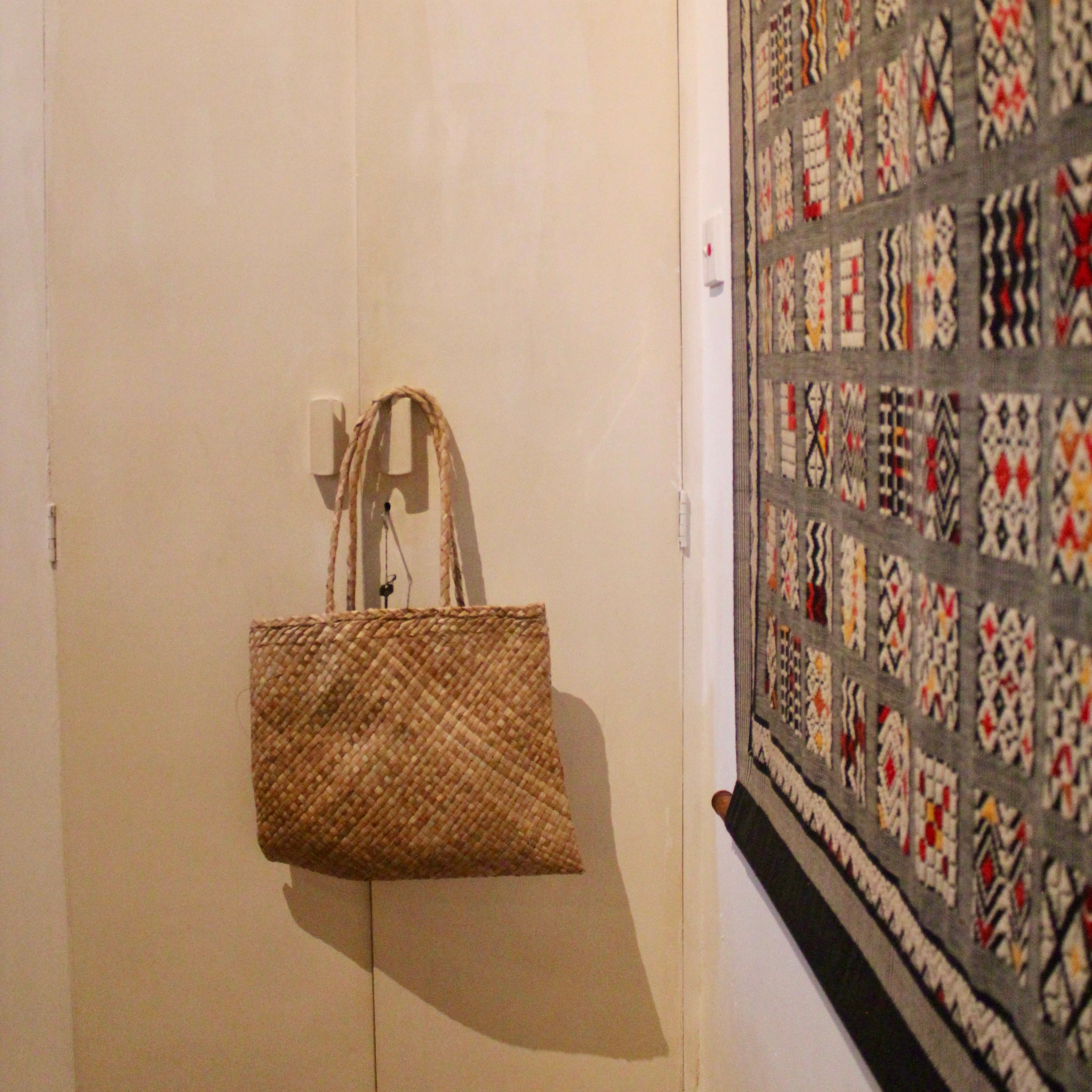 Woven bag hanging on a hook next to a quilt with geometric patterns.