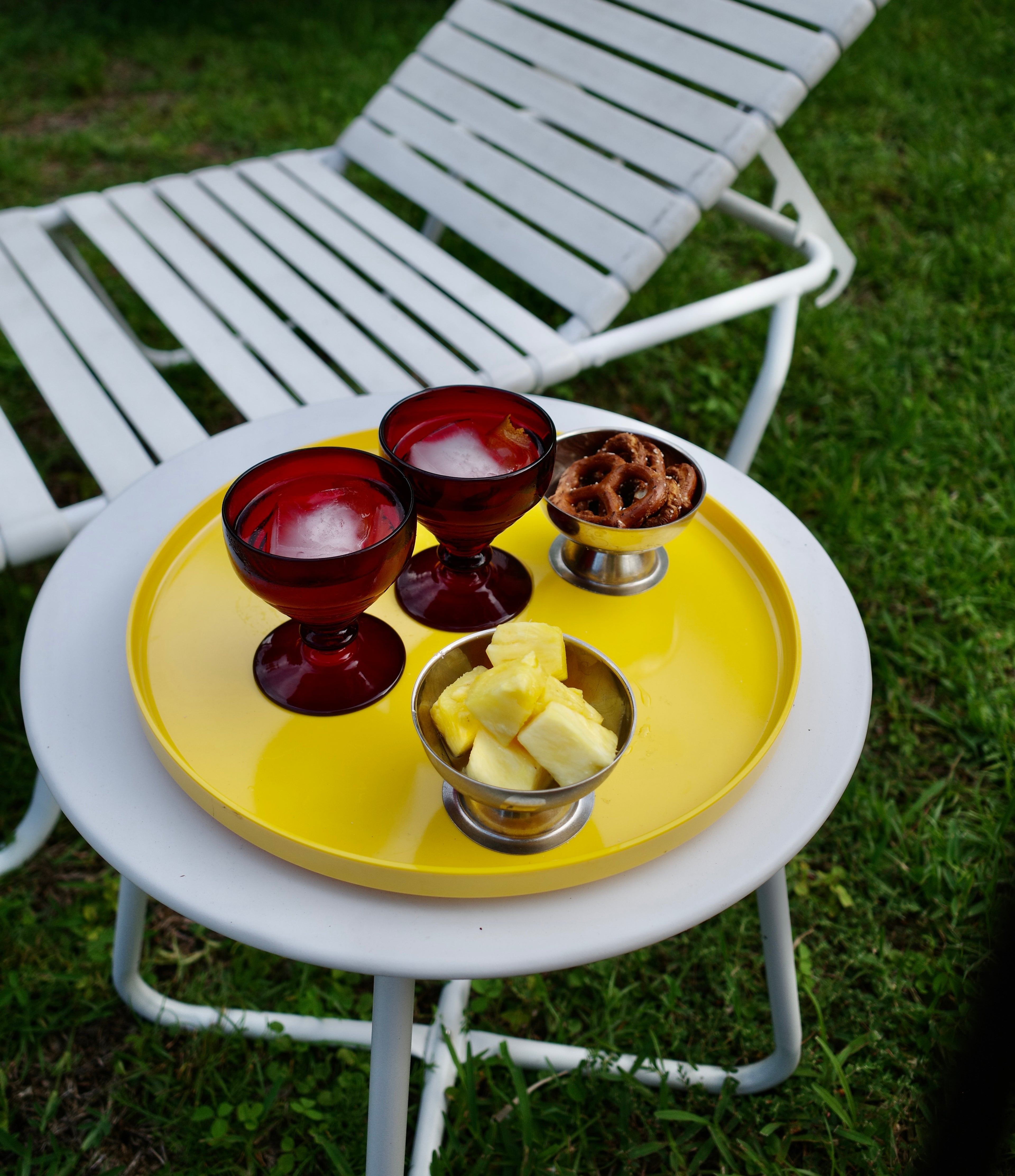 Yellow tray with red glass cups and small bowls on a white chair outdoors.